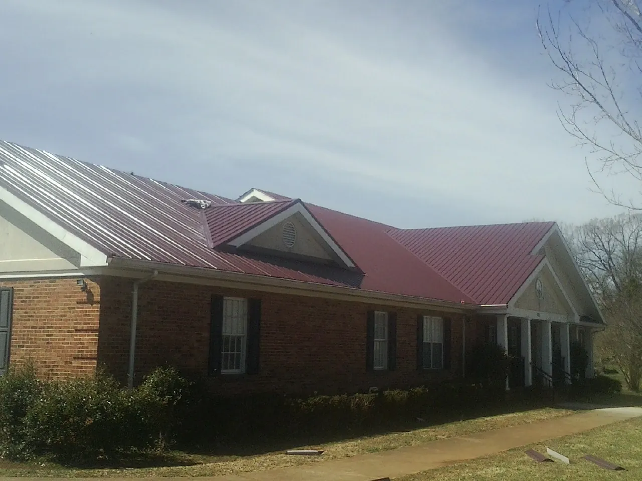 Red metal roof with gabled entries on a long brick building, from a Hail Damage Roof Repair job in Brentwood