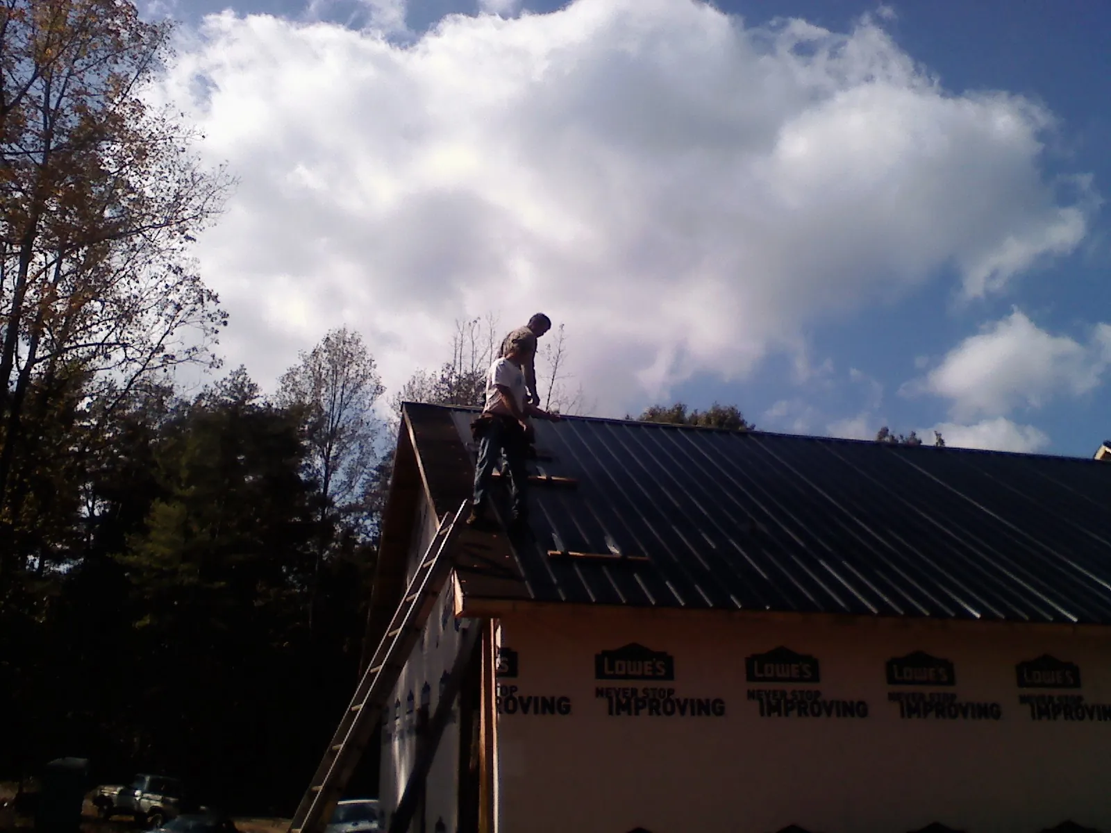 Roofer fastening dark metal panels high against a cloudy sky, from a Roof Inspection job in Brentwood