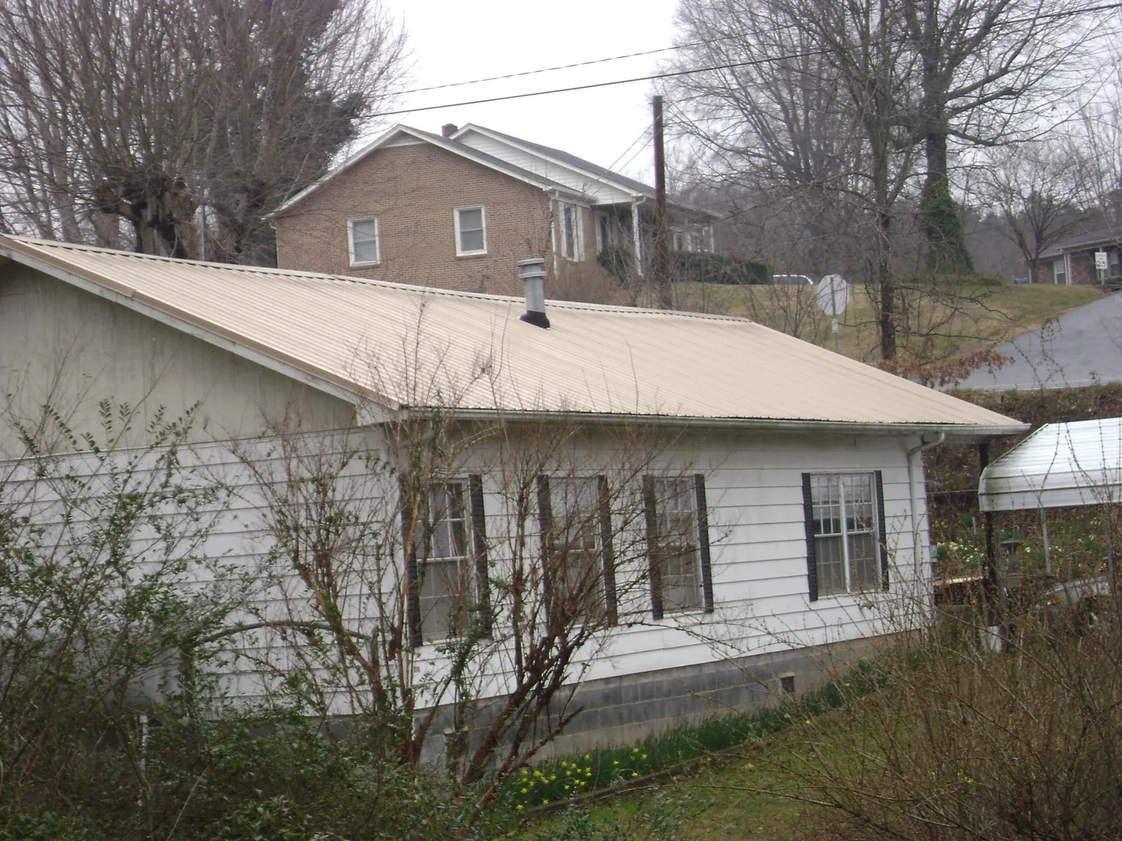 Tan metal roof on a white sided house set into a hillside — Commercial Roofing by Roofing Brothers in Brentwood